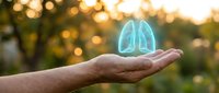 Glowing blue lungs hologram floating above open palm with warm bokeh lights background representing respiratory health and medical care concept.