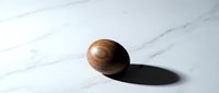 Wooden sphere with natural grain texture casting shadow on white marble surface for minimalist design projects and modern decor concepts.