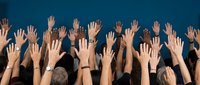Group of diverse people raising hands up against blue background showing unity, participation and engagement in community event or meeting.
