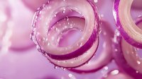 Sliced red onion rings with water droplets on pink background, fresh culinary ingredient for salads and cooking.