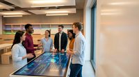 Diverse business team collaborating around interactive digital table in modern office meeting room with wooden shelving and contemporary design.