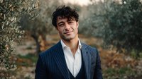 Young confident businessman in pinstripe suit smiling outdoors in natural garden setting with olive trees background for corporate and professional use.