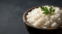 Cooked white rice in wooden bowl garnished with fresh parsley on dark background for healthy meal preparation and cooking concepts.