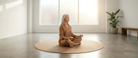 Young blonde woman in beige outfit practicing meditation in minimalist modern interior with natural light and plant for wellness and mindfulness concepts.