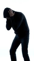 Anonymous man in black hoodie covering face with hand showing shame, guilt or depression isolated on white background for mental health concepts.