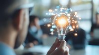 Glowing light bulb with digital icons floating around it held by business professional, representing innovation and creative technology solutions.