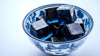 Black ice cubes in traditional blue and white porcelain bowl. Cool toned minimalist composition with frozen water blocks showing crystalline structure. Suitable for beverage and cooling concepts.