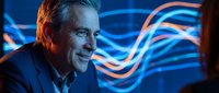 Mature man with light skin tone and gray hair wearing business attire, smiling against glowing neon blue and red wave light trails, suitable for tech, innovation, and corporate concepts.