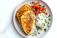 Grilled chicken breast with fresh tomato salsa and sour cream garnished with chopped parsley served on white plate, overhead view of protein-rich meal.
