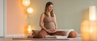 Young pregnant woman in beige loungewear sitting cross-legged on floor with warm ambient lighting, maternity wellness and prenatal care concept.