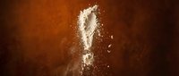 White flour exclamation mark symbol bursting with powder explosion on warm brown background for baking and cooking concepts.
