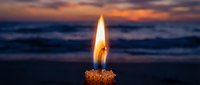 Burning candle flame glowing against dramatic ocean sunset with purple and orange sky colors creating peaceful meditation atmosphere for relaxation and mindfulness.