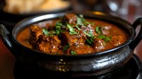 Aromatic chicken curry with tender meat pieces in rich orange-brown gravy garnished with fresh cilantro leaves, served in traditional black clay pot. Perfect for menu design.