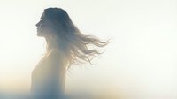 Young woman with flowing hair in golden sunlight creating dreamy silhouette against bright background for wellness and freedom concepts.