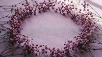 Purple baby's breath flowers arranged in circular wreath frame on soft lavender fabric background creating romantic floral border with copy space center.