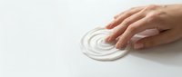 Hands applying white moisturizing cream or lotion on white surface, skincare and cosmetic product demonstration for beauty and wellness.