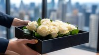 Elegant white roses arranged in modern black box against urban cityscape backdrop, hands holding luxury floral gift with Manhattan skyline view through window.