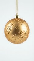 Golden Christmas ornament with snowflake patterns and swirl designs hanging on chain against white background for holiday decorations and festive displays.