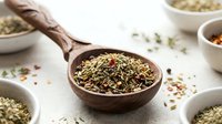 Aromatic herb blend with dried spices in wooden spoon surrounded by ceramic bowls on textured surface for culinary seasoning and cooking applications.