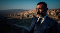Middle-aged businessman with beard in navy pinstripe suit gazing thoughtfully at panoramic city view during golden hour. Professional portrait for corporate marketing.