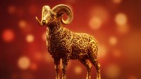 Golden ram figurine with curved horns standing against warm red and orange bokeh background with glowing light effects.