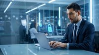 Professional businessman working on laptop with cybersecurity holographic interface displaying data protection and secure network icons in modern office.