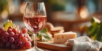 Glass of rosé wine with cheese and grapes on wooden board creating elegant dining atmosphere for restaurant menus and culinary content.