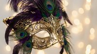 Ornate golden venetian carnival mask with peacock feathers and intricate metalwork against warm bokeh lights for masquerade party celebrations.