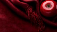 Red ripe apple on luxurious burgundy silk fabric with decorative fringe, creating dramatic contrast and elegant composition for food and fashion concepts.