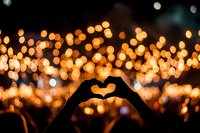 Silhouette of hands forming heart shape against blurred golden bokeh lights background at night concert or festival, romantic moment captured.