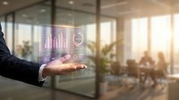 Businessman holding glowing holographic data analytics dashboard with charts and graphs in modern office environment with colleagues working in background.