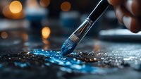 Artist paintbrush applying vibrant blue acrylic paint on textured canvas surface with warm bokeh lights creating atmospheric creative workspace ambiance.