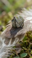 Miniature wooden house model sitting on feather in natural outdoor setting symbolizing home dreams, real estate investment, and property ownership aspirations.