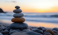 Balanced stack of smooth zen stones on beach pebbles against golden sunset and ocean waves, creating peaceful meditation atmosphere at tranquil seashore.