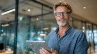 Confident mature businessman with glasses using digital tablet in modern office space, innovative technology concept visualized with light particles.
