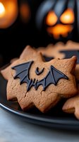 Halloween bat cookies with chocolate wings on dark plate with spooky jack-o-lantern background for autumn baking and seasonal treats.