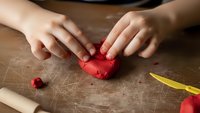 Child hands molding red clay on wooden table during art craft activity session for creative learning and development.