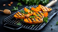 Grilled sweet potato slices with grill marks on black iron grate, garnished with fresh herbs and honey drizzle against dark background, food photography.