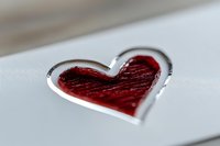 Red heart shape with metallic silver border on white surface, macro photography showing textured detail and romantic symbolism for love and affection.