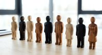 Diverse wooden figurines representing different ethnicities and genders standing in row on office desk symbolizing workplace diversity and inclusion concepts.