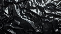 Crumpled black plastic material with dramatic shadows and highlights creating abstract textural pattern. Suitable for modern design backgrounds and artistic projects.