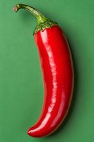 Fresh red chili pepper with green stem isolated on green background, showing natural texture and glossy surface for food and cooking concepts.
