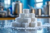 White sugar cubes stacked in pyramid formation on blue surface with scattered granulated sugar, soft focus background creates dreamy atmosphere for food photography.