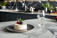 Elegant panna cotta dessert with fresh berries and mint leaf on gray plate, served on marble countertop with empty wine glass in modern kitchen setting.