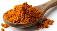 Vibrant orange turmeric powder heaped in wooden spoon against white background, scattered aromatic spice grains showing texture and natural color for cooking and wellness.