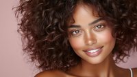 Young mixed-race woman with curly hair smiling at camera against pink background. Natural beauty portrait for lifestyle and wellness campaigns.