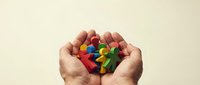 Cupped hands holding colorful wooden human figures representing diversity, teamwork and community support in social care and inclusion concepts.