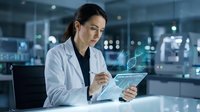 Female scientist in white lab coat analyzing data on tablet in modern laboratory. Professional researcher conducting medical research in high-tech facility.