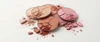Broken makeup powder compacts in warm nude and pink tones scattered with crumbled cosmetic powder on white background for beauty and fashion projects.