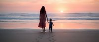 Mother and child walking hand in hand on beach at sunset with golden sky and ocean waves. Family bonding moment during peaceful evening stroll by the sea.